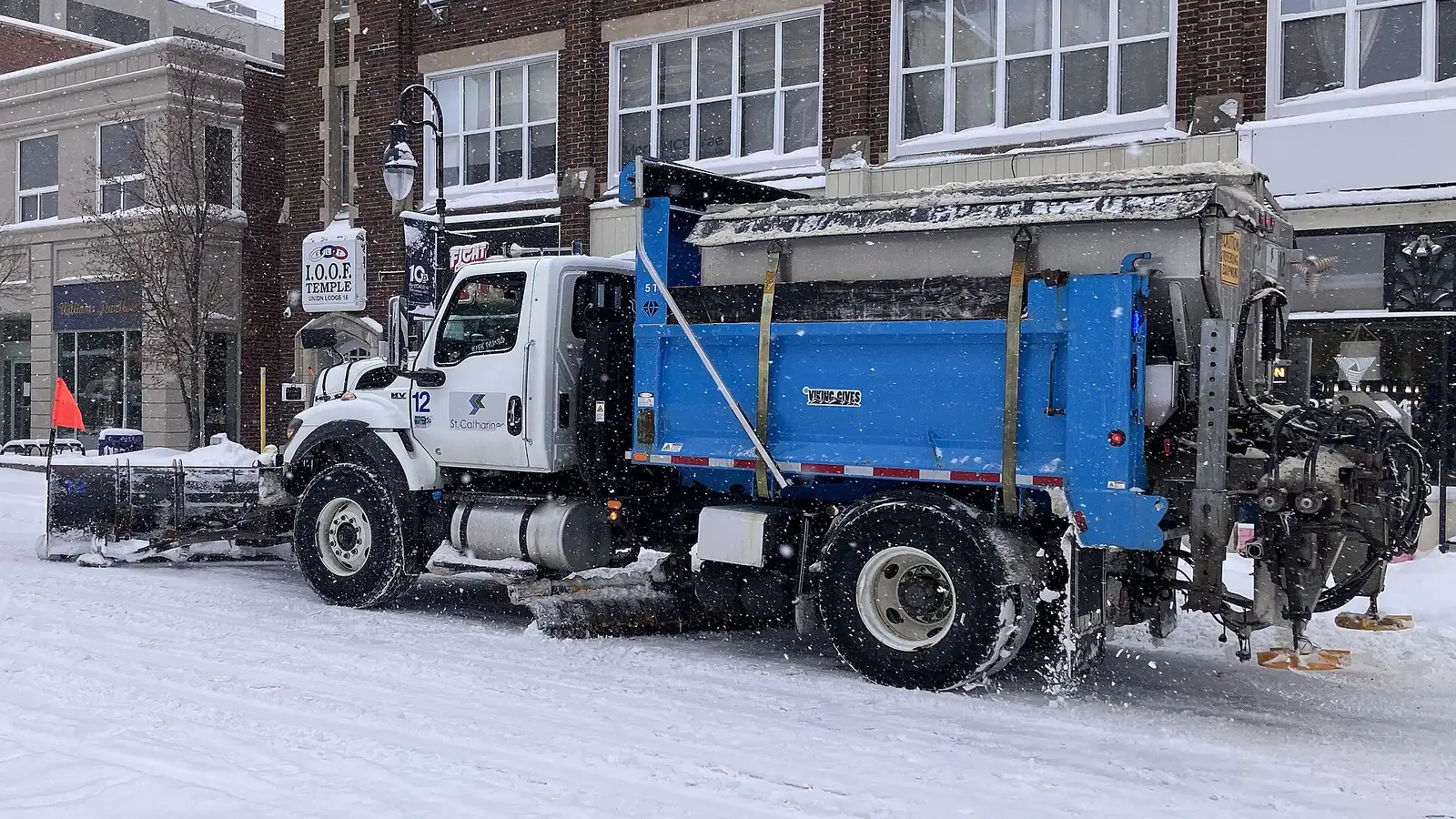 White and blue snow plow truck on a snowy street